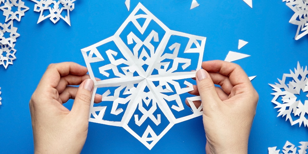 Hands crafting a snowflake from a piece of white paper